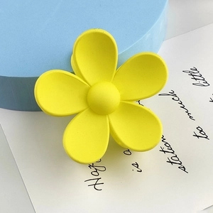 Macro view of matte yellow flower hair claw clip with spring hinge on a blue display base