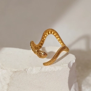 Close-up of golden snake ring with detailed scale texture resting on a white rock