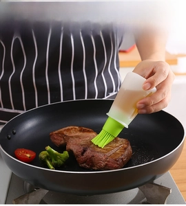 Silicone oil brush bottle with scale applying oil to steak in a cooking pan