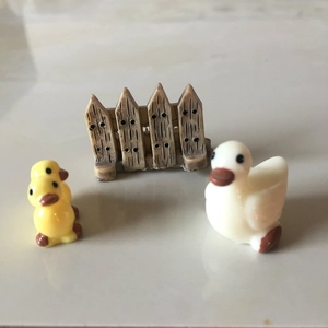 Miniature resin set with yellow and white ducks by a brown garden fence detail