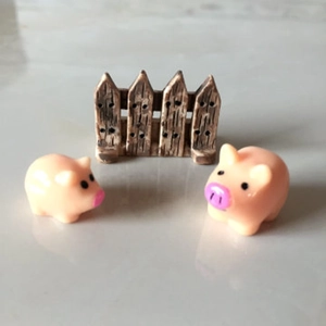 Detail shot of miniature resin pig figurines with a faux wood fence on a white surface