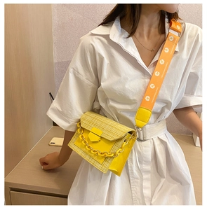 Detail of yellow woven crossbody bag with orange daisy strap and metal chain on model