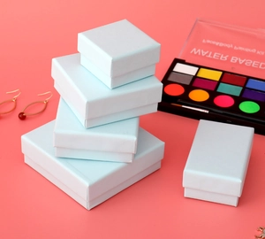 Various sizes of light blue cardboard jewelry gift boxes stacked on a pink background