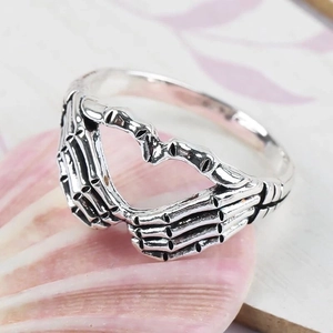 Vintage silver skeleton hand heart ring with gothic punk aesthetic on a shell background