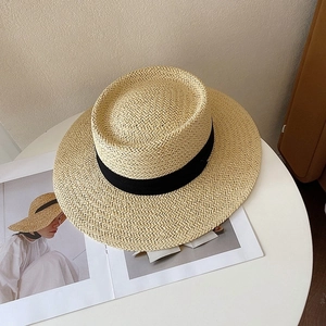 Close-up of a woven straw boater hat with a black ribbon on a minimalist white table