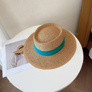 Detailed top view of a flat top straw sun hat with a blue ribbon on a white table
