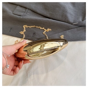 Detailed view of an oval gold acrylic clutch bag with a polished finish and chain strap
