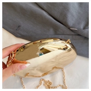 Detail of a luxury gold metallic acrylic box clutch with a polished mirror finish and chain