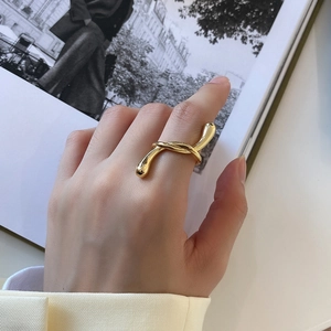 Close-up of golden twisted streamline ring on model hand with fashion magazine background