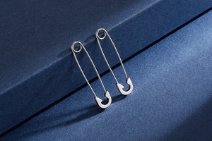 Close-up of silver safety pin earrings on a blue textured background with sharp shadows