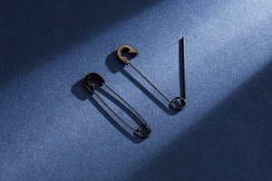 Detail view of matte black safety pin earrings on dark blue fiber background texture