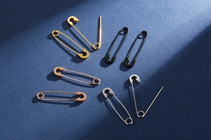 Safety pin earrings in gold, black, rose gold, and silver on a dark blue background