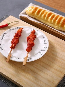 Close-up of grilled meat skewers served on greaseproof baking paper in a white plate
