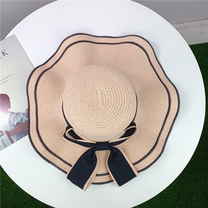 Beige wide-brimmed straw sun hat with a black bow and wavy piping for beach travel