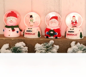 Close-up of four glowing Santa and snowman crystal balls with Merry Christmas base