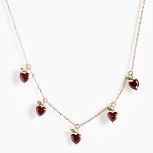 Detail shot of heart-shaped red cherry pendants with green crystals on a gold chain