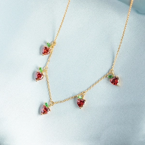 Detail of gold necklace with five red and green crystal fruit charms on blue silk