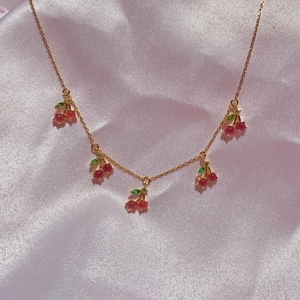 Detailed close-up of cherry pendants with red crystals and green gems on a gold chain