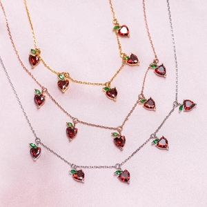 Detailed view of cherry pendants in gold, rose gold, and silver on pink silk fabric