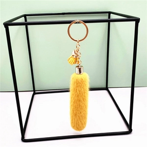 Yellow plush tassel keychain with golden metal ring hanging in a geometric black frame