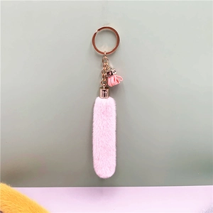 Close-up of pink plush keychain with golden ring and matching tassel on a dual-tone background