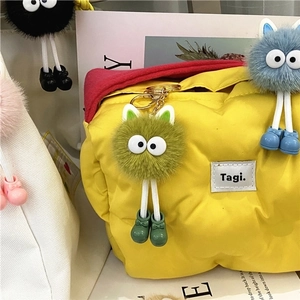 Close-up of colorful fuzzy ball keychains with long legs on a yellow quilted puffy bag