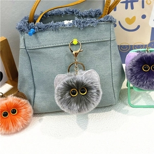 Detailed view of fluffy cat plush keychain with gold metal clasp on a denim bag