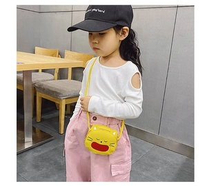Toddler girl wearing a bright yellow cartoon cat crossbody bag in a cozy indoor setting