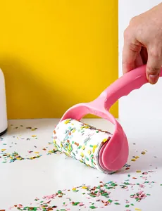 Action shot of pink lint roller picking up colorful debris on a bright tabletop