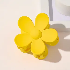 Close-up of bright yellow matte flower hair claw clip on warm beige background