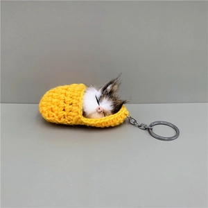 Macro detail of a plush sleeping cat keychain inside a yellow knit sleeping bag charm