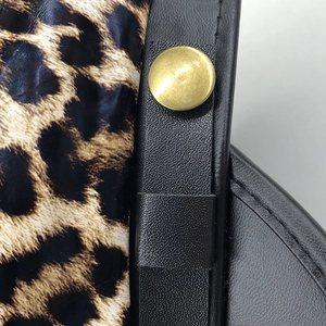 Macro shot of leopard print fabric with black leather trim and a gold metal snap button