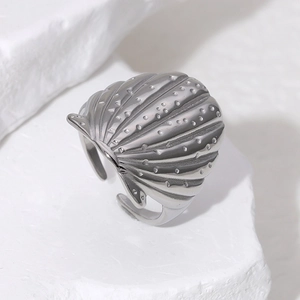 Detailed view of ocean-style shell-shaped stainless steel ring on a white stone base