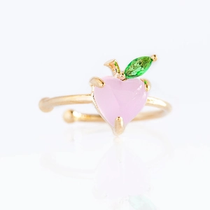 Detailed close-up of gold open ring with peach-shaped pink heart and green leaf gems