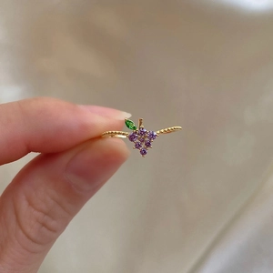 Detail of a gold-tone twisted ring featuring a grape cluster with purple and green stones