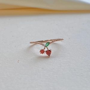 Detailed view of a rose gold cherry ring with green leaf and orange-red gemstones