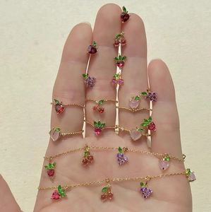Detail view of colorful fruit-shaped rings and jewelry set in gold finish on a hand
