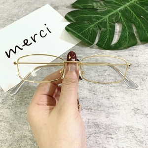 Detail of slim gold geometric metal sunglasses frame with grey ear tips held by hand