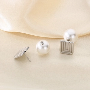 Macro shot of silver square earrings with white pearls on a beige silk fabric background