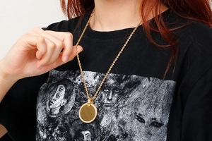 Detailed view of a gold circular pendant with crystal border and rope chain on a model
