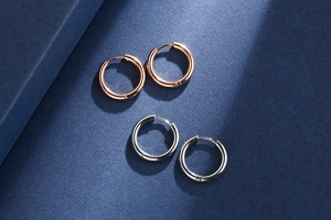 Detailed view of polished rose gold and silver stainless steel hoop earrings on blue paper