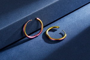 Close-up of rainbow gradient titanium hoop earrings on a textured blue surface