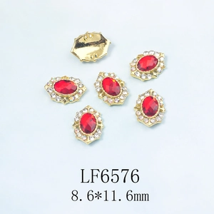 Détail macro du bijou d'ongle cristal rouge ovale avec base dorée et strass blancs
