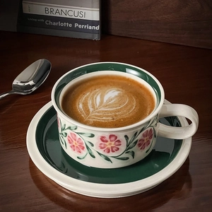 Detail of vintage hand-painted floral ceramic coffee cup set with latte art on wood table