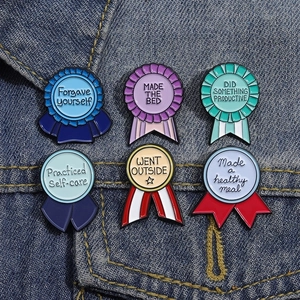 Set of six colorful enamel award ribbon pins with motivational phrases on denim jacket