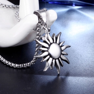 Detailed view of silver sun pendant on a box chain held by a mannequin hand