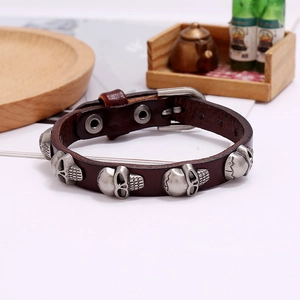 Close-up of punk style dark brown leather bracelet with five silver skull charms