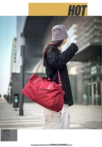 Deep red oversized travel bag worn by a model in a modern urban street setting