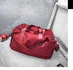 Detail of red travel duffel bag with handles and adjustable shoulder strap on concrete floor