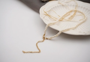 Detail of white mini freshwater pearl necklace with adjustable gold lobster clasp on ceramic